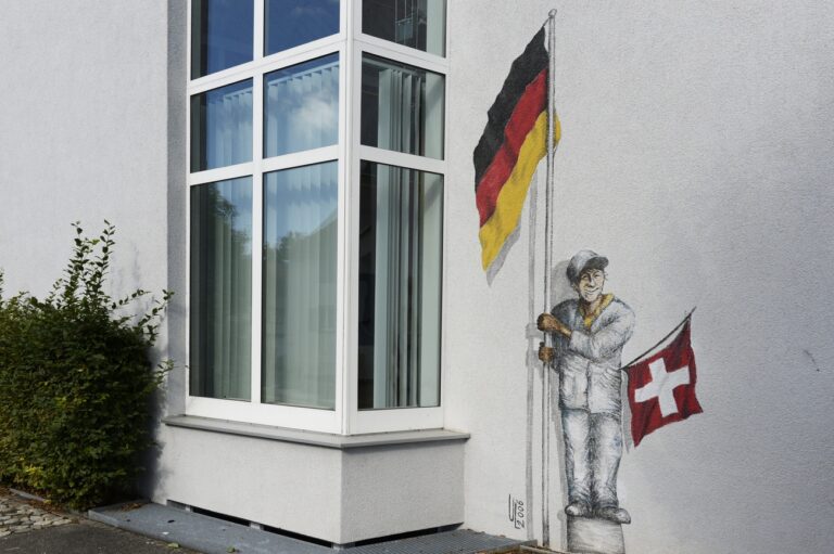 Eine Figur mit den Flaggen der Schweiz und Deutschlands ist auf eine Fassade gemalt, aufgenommen in Buesingen am Hochrhein am Donnerstag, 19. September 2013. Buesingen ist gaenzlich von Schweizer Staatsgebiet umgeben. Er grenzt rechtsrheinisch an den Kanton Schaffhausen und linksrheinisch an die Kantone Zuerich und Thurgau. Buesingen ist die einzige Gemeinde der Bundesrepublik Deutschland, die eine Exklave des Bundesgebietes bildet. (KEYSTONE/Steffen Schmidt) *** NO SALES, NO ARCHIVES ***