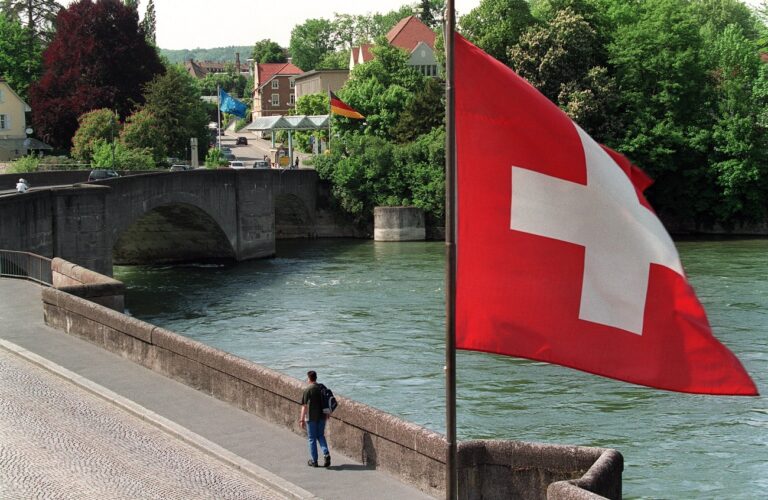 Die Schweizer Fahne, rechts, weht ueber den Rhein in Richtung Europa-Fahne, Hintergrund, aufgenommen am 11. Mai 2000 beim Schweizer Zoll bei Rheinfelden in Richtung Deutschland. In der Mitte ist die Deutschland-Fahne auszumachen. Die Freizuegigkeit im Personenverkehr soll schrittweise eingefuehrt werden. Die Schweiz kann nach sieben Jahren ueber eine Verlaengerung des Abkommens entscheiden. Das Abkommen gilt fuer Arbeitnehmer, Selbstaendigerwerbende und Personen ohne Erwerbstaetigkeit. Mehr als vier Jahre lang handelten die Schweiz und die EU die bilateralen Vertraege aus. Am 21. Mai 2000 stimmen Schweizerinnen und Schweizer ueber sieben Abkommen ab, welche das Verhaeltnis der Schweiz mit Europa in den Bereichen Personenverkehr, Landverkehr, Luftverkehr, technische Handelshemmnisse, oeffentliches Beschaffungswesen, Forschung und Landwirtschaft auf eine solide Basis stellen sollen. (KEYSTONE/Martin Ruetschi)