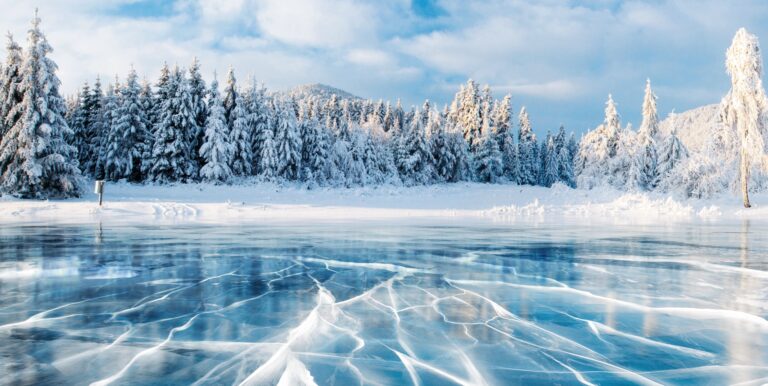 Blue ice and cracks on the surface of the ice. Frozen lake under a blue sky in the winter. The hills of pines. Winter. Carpathian, Ukraine, Europe.