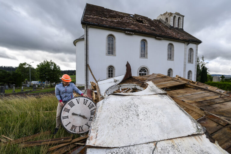 Maurice Bianchi, responsable de la creche aux 5 sens, constate les degats et decouvre le cadran du clocher du Temple des eplatures, un jour apres le passage de la forte tempete le mardi 25 juillet 2023 au Cret-du-Locle a cote de La Chaux-de-Fonds. Le deblaiement des materiaux et la reparation des infrastructures ont repris mardi a La Chaux-de-Fonds dans le canton de Neuchatel, apres la violente tempête de la veille. (KEYSTONE/Jean-Christophe Bott)