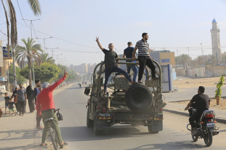 Palestinians ride on an Israeli military vehicle taken by an army base overrun by Hamas militants near the Gaza Strip fence, in Gaza City, Saturday, Oct. 7, 2023. (AP Photo/Abed Abu Reash)