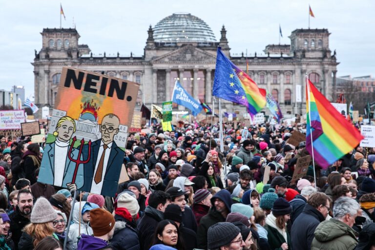 02.02.2025, Berlin: Eine Teilnehmerin hält ein Schild mit einem gemalten Bild von A. Weidel (AfD) und Friedrich Merz (CDU) mit einem brennenden Reichstagsgebäude und der Aufschrift 