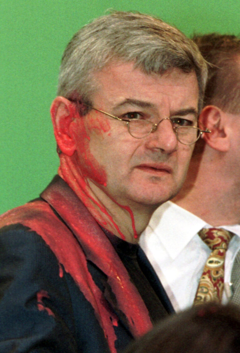 ARCHIV - 13.05.1999, Deutschland, Bielefeld: Farbverschmiert steht der damalige Bundesauﬂenminister Joschka Fischer auf der B¸hne beim Gr¸nen-Sonderparteitag in der Seidensticker-Halle. Fischer war von einem Demonstranten aus Protest gegen seine Kosovo-Politik mit einem Farbbeutel beworfen worden. Nach fast 20 Jahren holt die Bundeswehr im Feldlager in Prizren die Flagge ein. (zu dpa-Story 